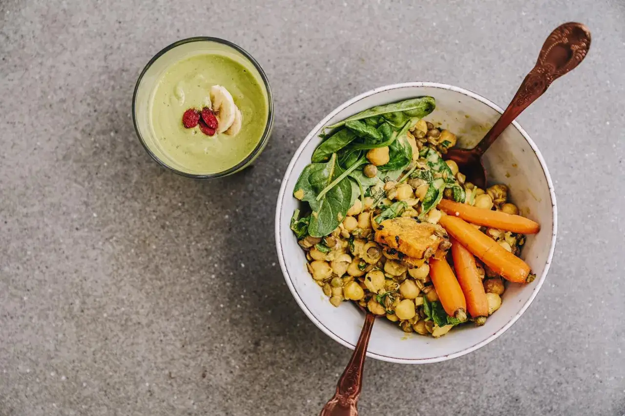 Miseczka z ciecierzycą z puszki, soczewicą, szpinakiem i marchewką. Obok zielony koktajl z bananem. Czy ciecierzycę z puszki trzeba gotować? Nie, jest gotowa do spożycia!