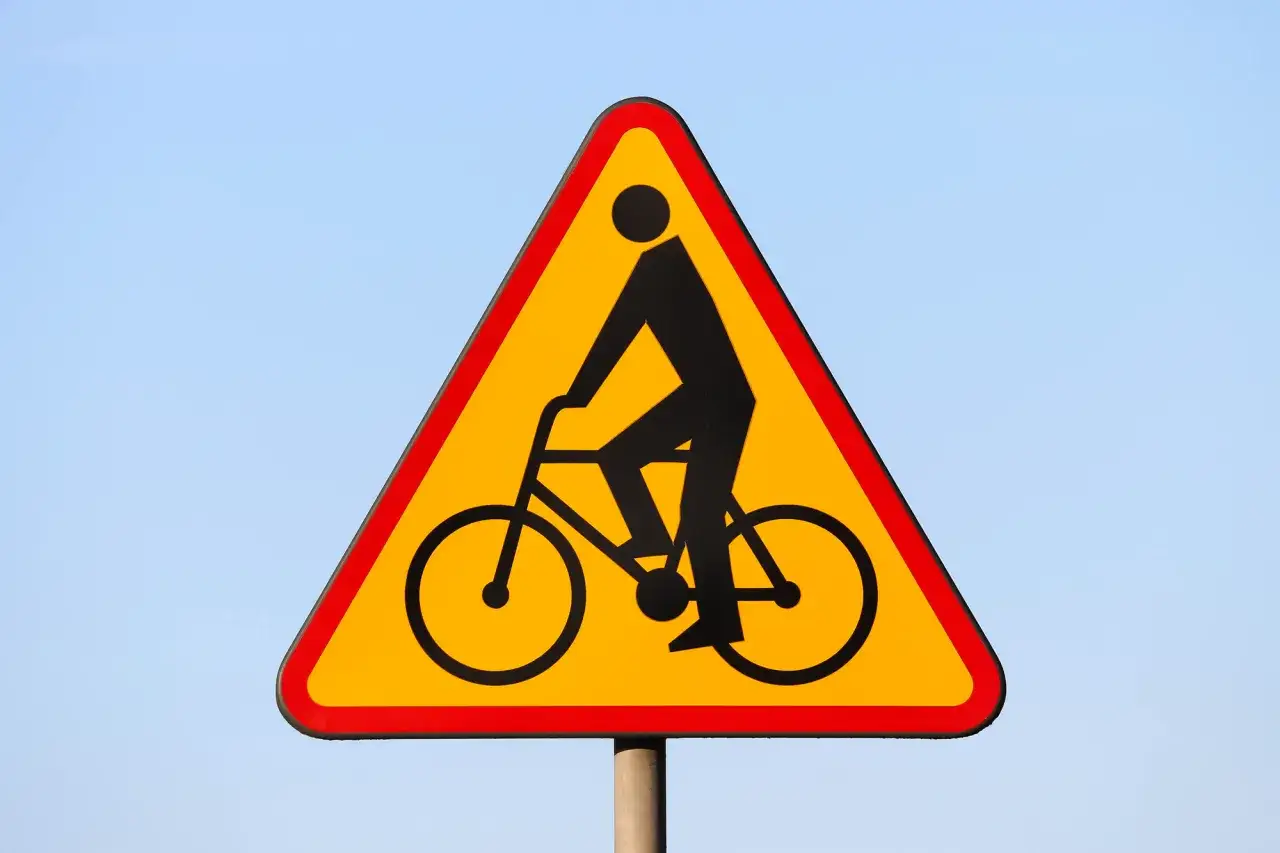 Znak ostrzegawczy: uwaga, rowerzyści! Czy bez karty rowerowej można jeździć po chodniku? Ten znak sugeruje, że tak, ale zawsze warto sprawdzić przepisy.