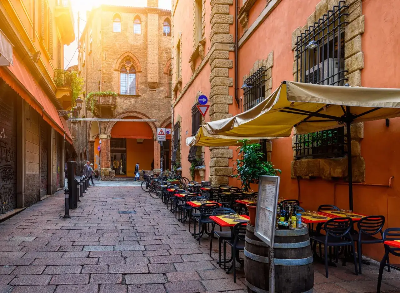 Urokliwa uliczka w Bolonii, gdzie zjesc można w jednej z wielu restauracji z ogródkiem. Słoneczny dzień zachęca do posiłku na świeżym powietrzu.