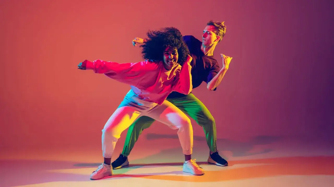 Dwoje tancerzy w dynamicznych pozach, oświetlonych neonowym blaskiem. Ich ruchy opowiadają historię tańca, niczym na maturze z pasji.