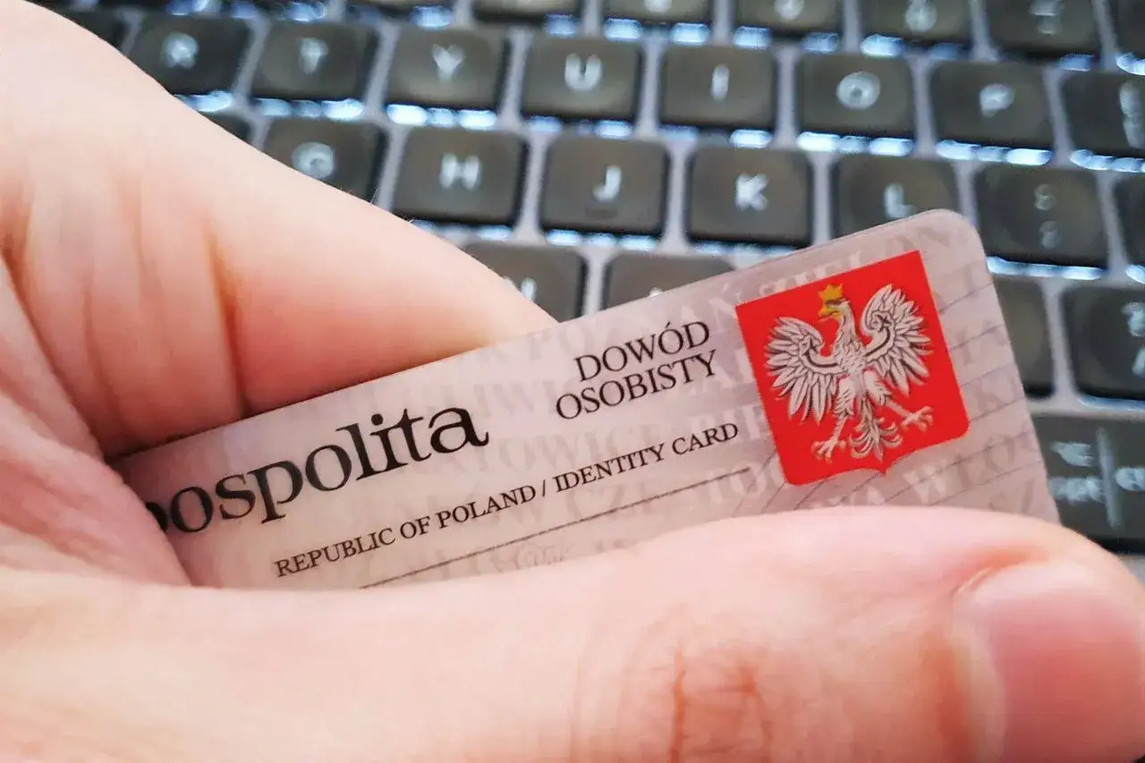 Dłoń trzyma dow&oacute;d osobisty na tle klawiatury. Chroń swoje dane, by jak uniemożliwić wzięcie pożyczki na nie.