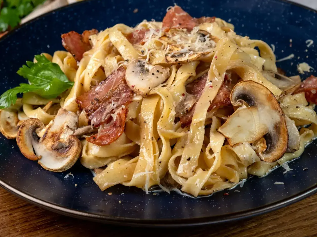 Pyszny makaron z boczkiem, grzybami i parmezanem na granatowym talerzu.