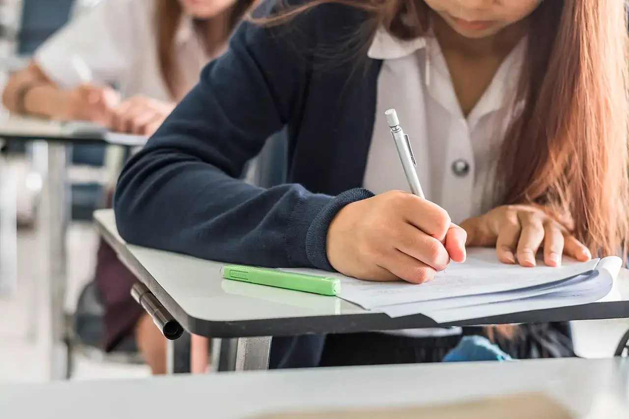 Uczennica pisze wypracowanie na egzaminie w liceum. Skupiona, z długopisem w dłoni, walczy o jak najlepszy warunek w liceum.