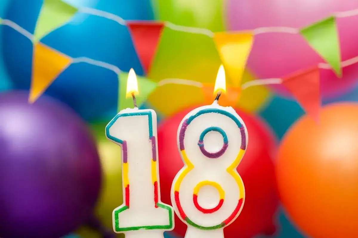 Świeczki z cyframi 1 i 8, płonące na tle kolorowych balonów i chorągiewek. Idealne na imprezę osiemnastkową!