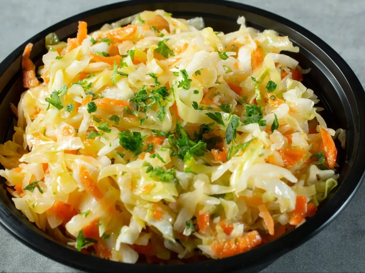 Świeża sur&oacute;wka z białej kapusty z marchewką i natką pietruszki, podana w czarnej misce.