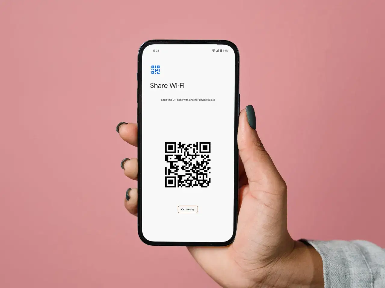 Dłoń trzyma smartfon z kodem QR do udostępniania Wi-Fi. To klucz zabezpieczeń sieciowych w telefonie, ułatwiający połączenie.