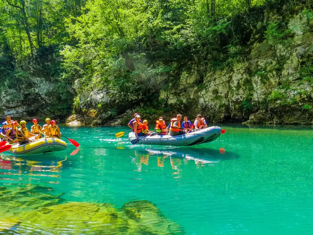 Rafting na turkusowej rzece w Czarnogórze we wrześniu. Grupa turystów w kamizelkach ratunkowych płynie pontonem wśród zielonych, skalistych brzegów.