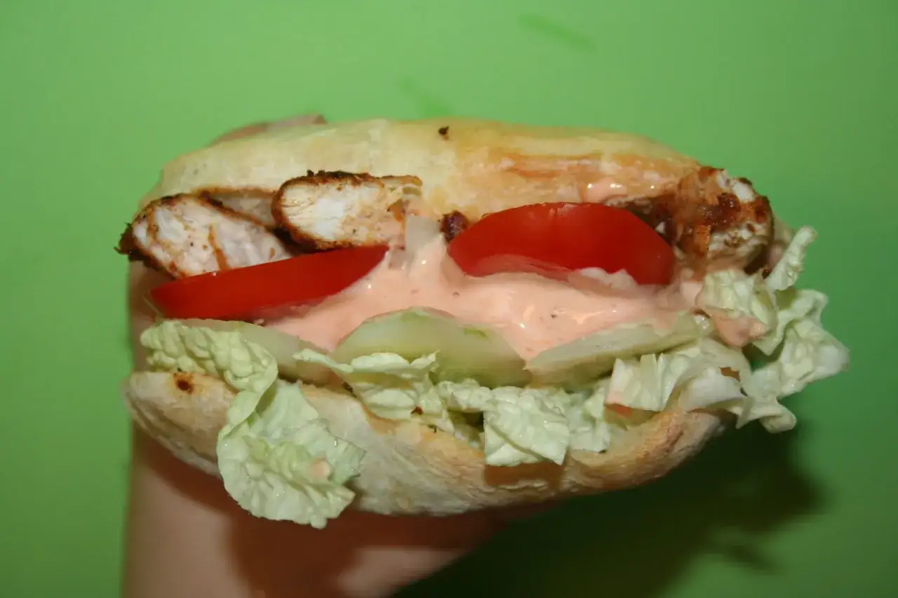 Pyszny kebab z kurczakiem, pomidorami, ogórkiem i sałatą, polany kremowym sosem mieszanym do kebaba.