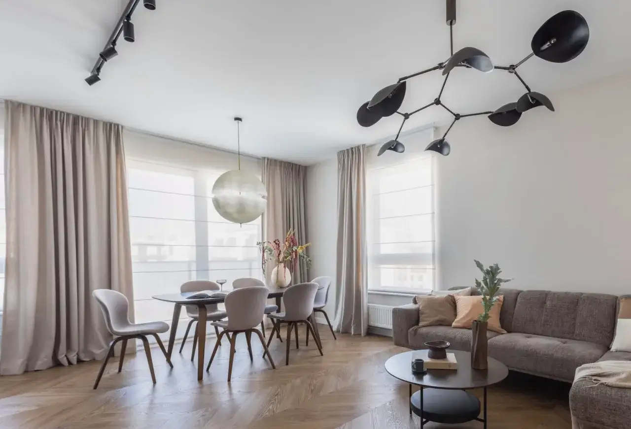 Nowoczesne oświetlenie salonu z jadalnią: designerska lampa nad stołem i reflektory na suficie tworzą przytulną atmosferę.