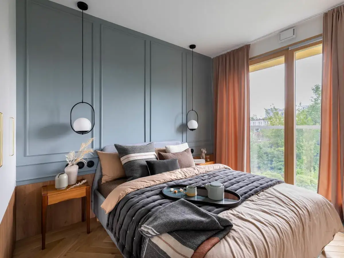 Nowoczesne oświetlenie sypialni inspiracje: wiszące lampy nad ł&oacute;żkiem, pastelowe ściany i zasłony tworzą przytulną atmosferę.