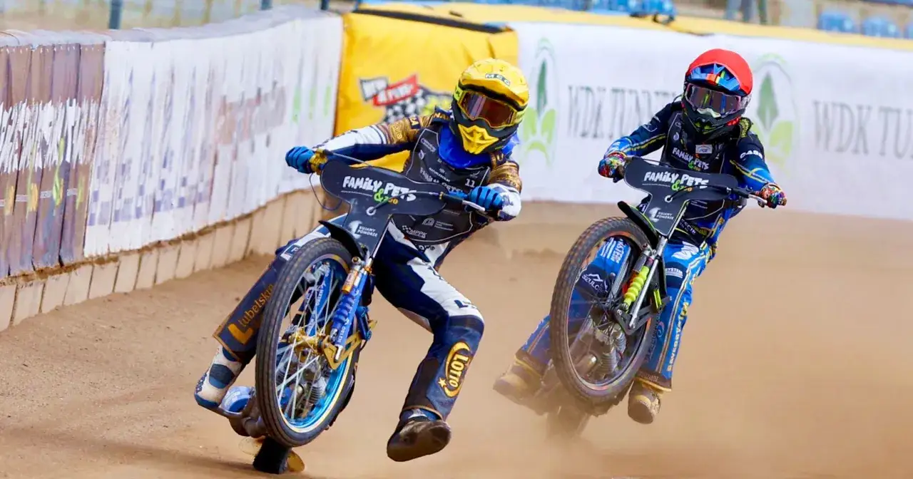 Dwóch zawodników żużlowych ściga się na torze, walcząc o punkty w PGE Ekstralidze. Ich pędzące motocykle wzbijają tumany kurzu, a każdy zakręt to walka o ułamki sekund.