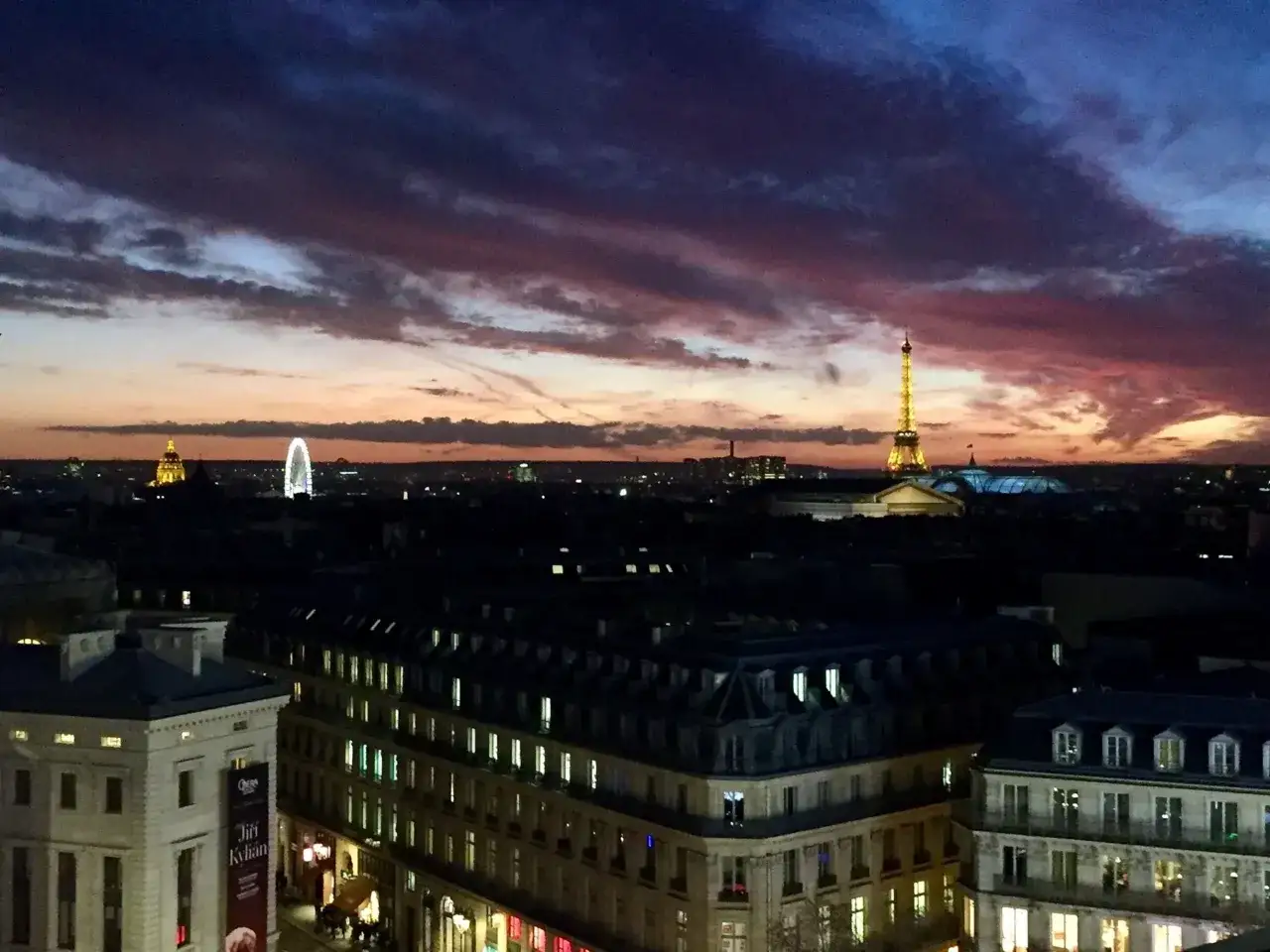 Zachód słońca nad Paryżem, widok na Wieżę Eiffla i inne budynki. W oddali widać diabelski młyn. To piękny widok z 9 dzielnicy Paryża.