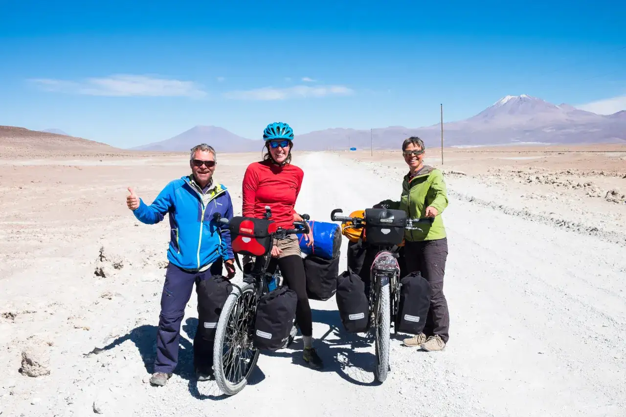 Trzech rowerzystów na pustkowiu w Boliwii, z wulkanem w tle. Boliwia słynie z surowych krajobrazów i przygód.