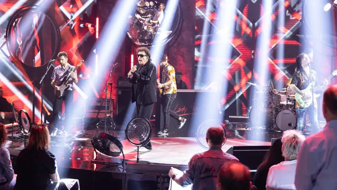 Zespół Lady Pank na scenie, grający swoje hity. Wokalista w okularach śpiewa do mikrofonu, gitarzyści i perkusista tworzą energetyczną atmosferę.
