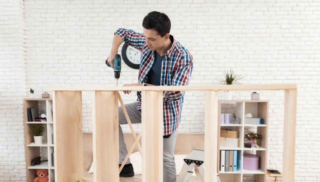 Mężczyzna skręca meble, zastanawiając się, ile kosztuje skręcanie mebli. W tle regały z książkami i dekoracjami.