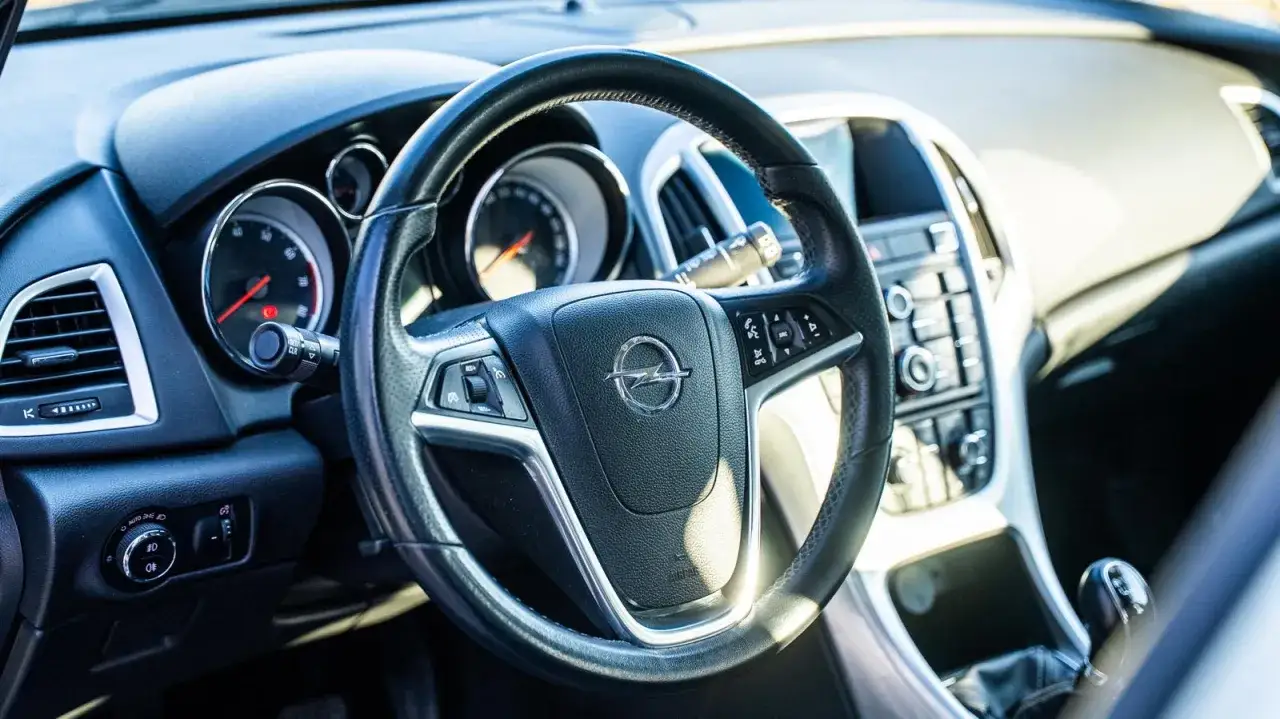 Wnętrze Opla Astry J z widoczną kierownicą, deską rozdzielczą i dźwignią zmiany biegów.
