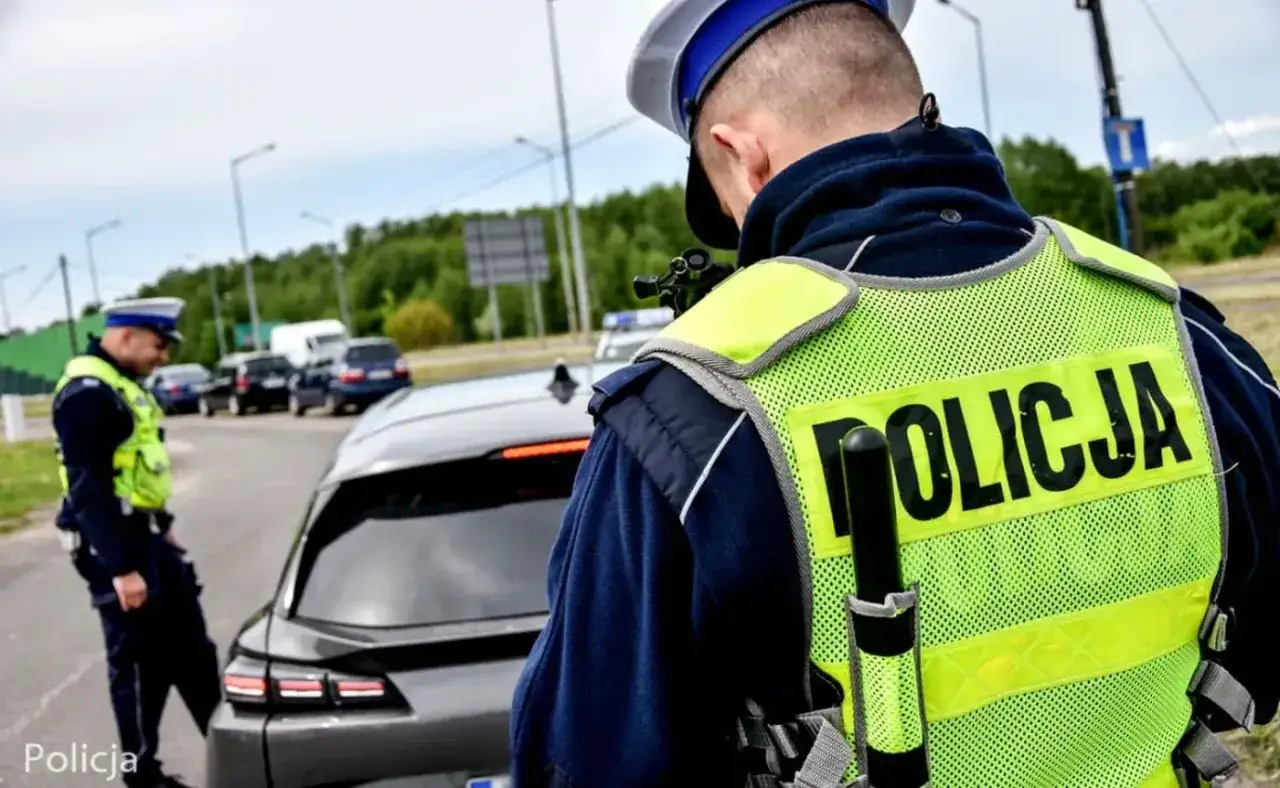 Policjant w kamizelce odblaskowej kontroluje kierowcę. Grozi mu mandat za brak prawa jazdy.