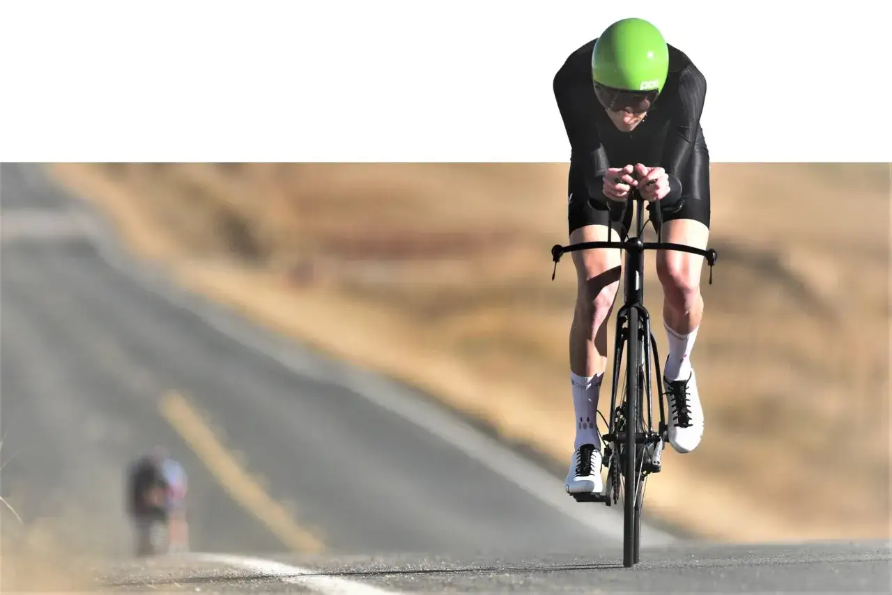 Kolarz w zielonym kasku pędzi po pustej drodze. Dobre suplementy dla kolarzy pomagają osiągać takie wyniki.