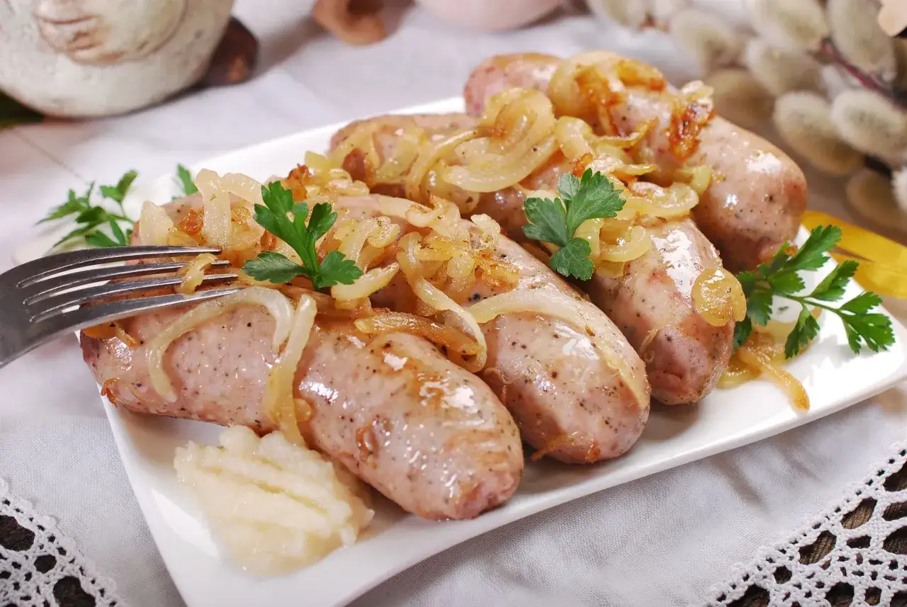 Słuchaj, ile czasu parzyć surową kiełbasę? Na talerzu pyszne, rumiane kiełbaski z cebulką i puree.