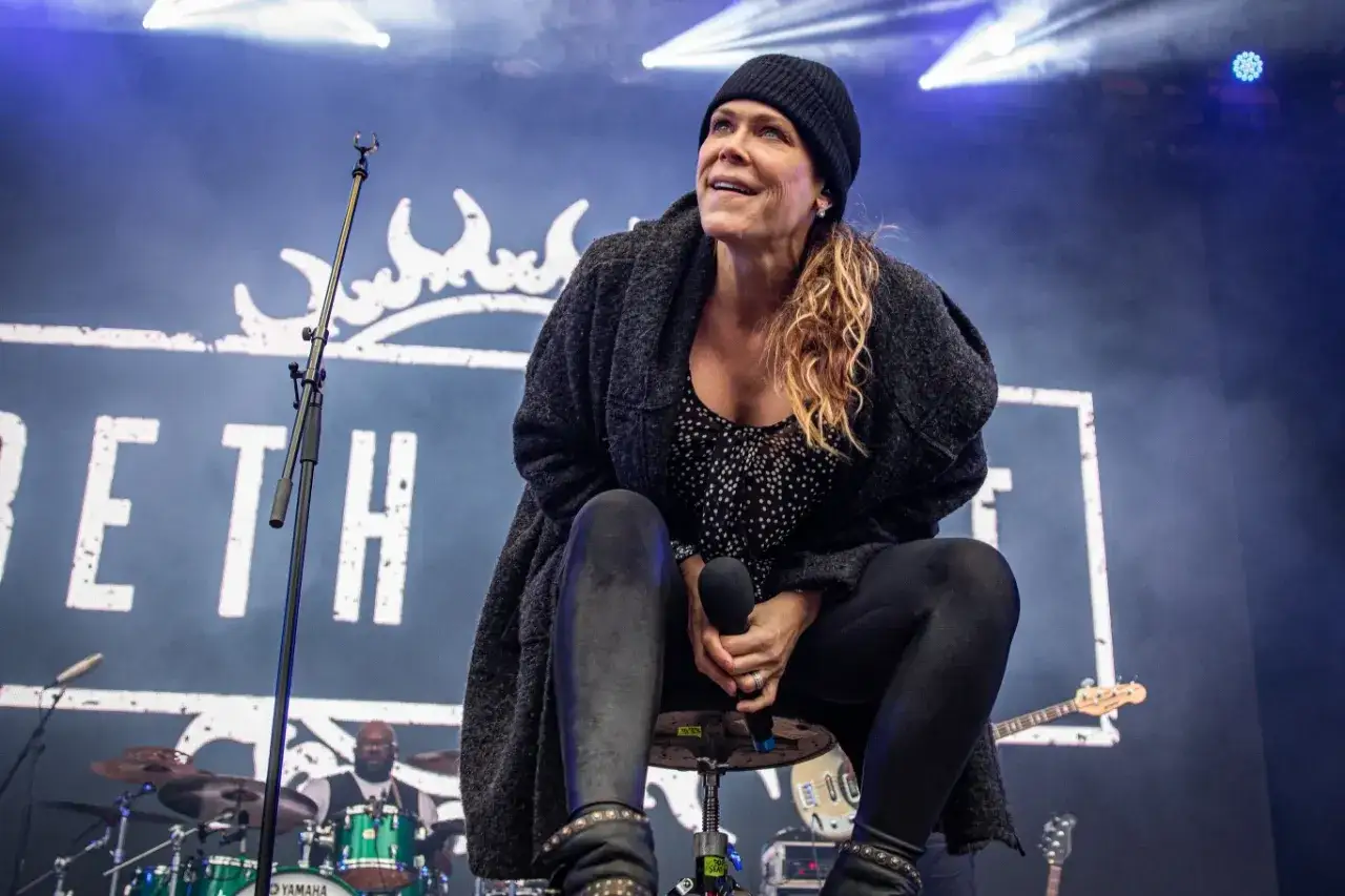Beth Hart na scenie, w czapce i płaszczu, śpiewa z pasją. Jej muzyka porusza serca, jakby opowiadała historie o swoich dzieciach.