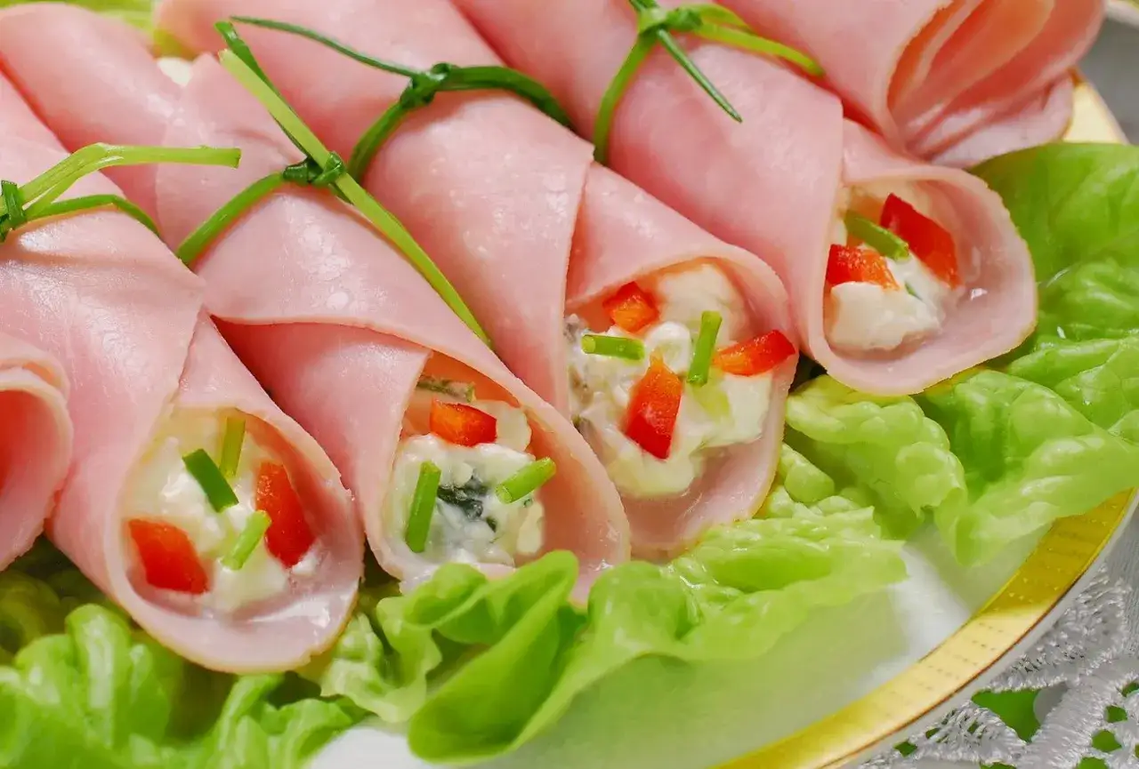 Roladki z szynki z kremowym nadzieniem, papryką i szczypiorkiem, ozdobione zieloną trawką.