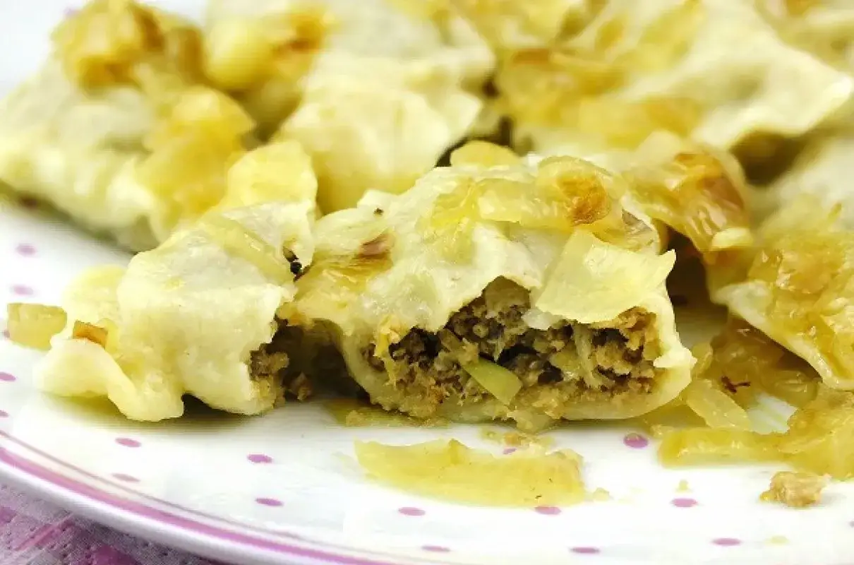 Pyszne pierogi z mięsem i kapustą, jeden rozkrojony, ukazujący bogate nadzienie.