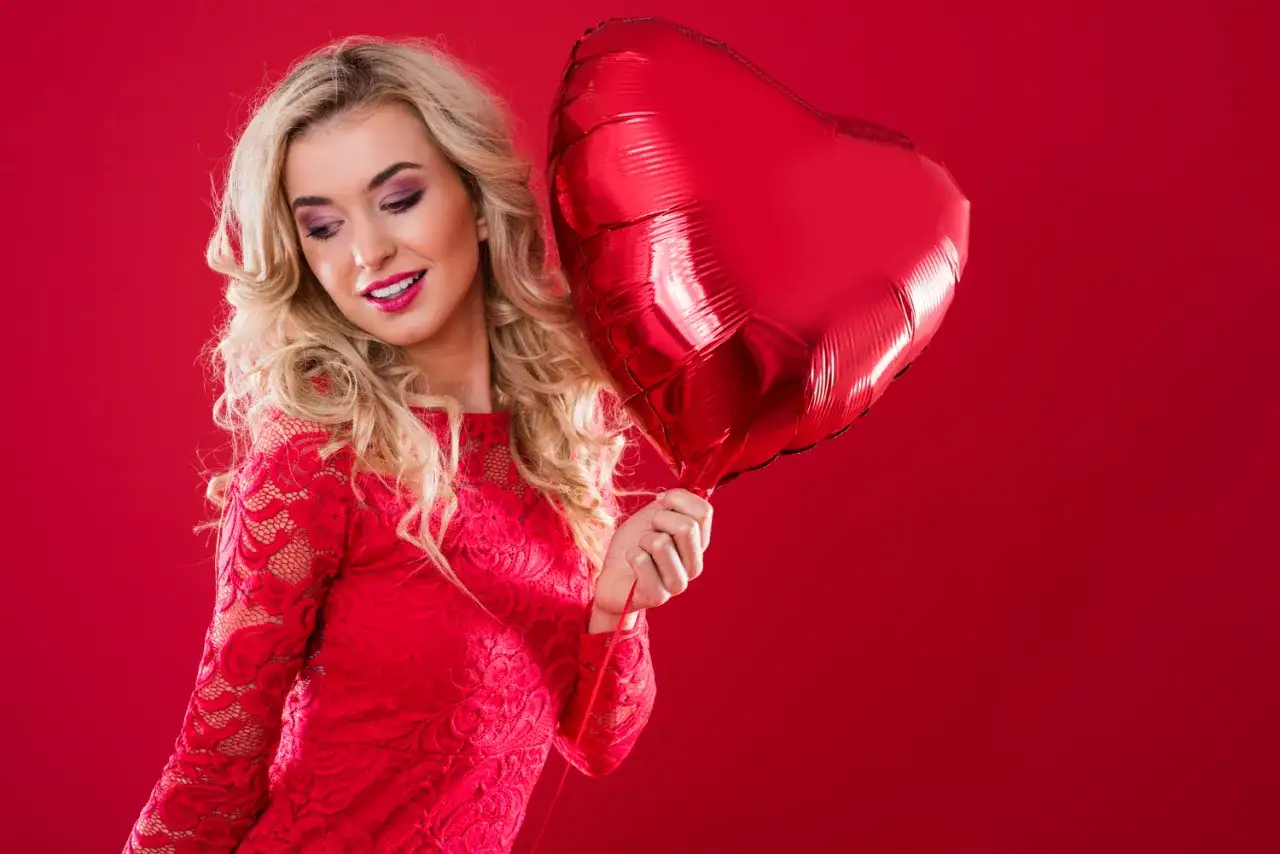 Kobieta w czerwonej koronkowej sukience trzymająca czerwone serce-balon. Idealny sposób, jak podniecić męża.