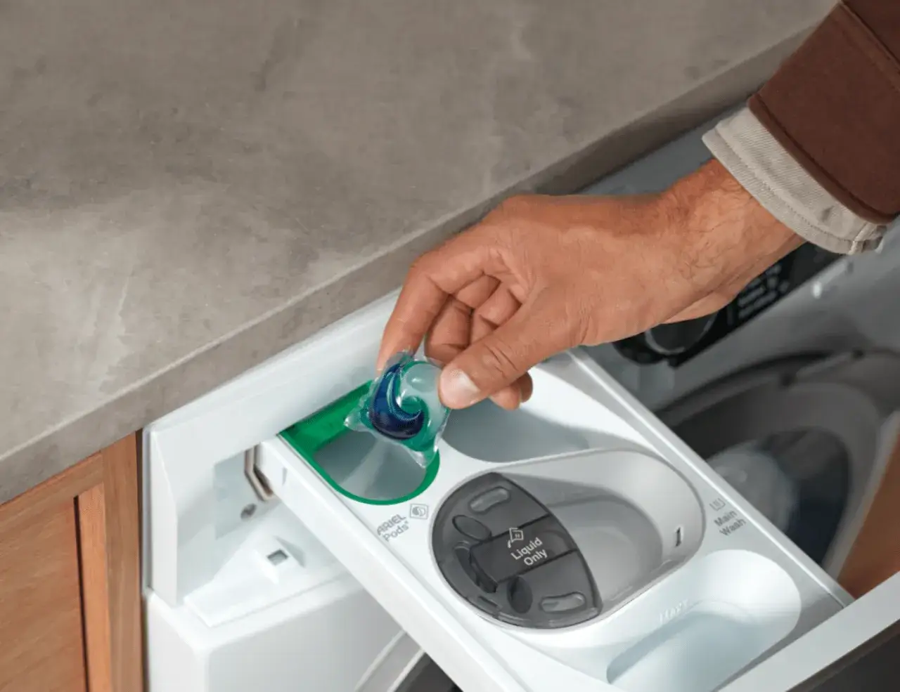 Dłoń wkłada kapsułkę Ariel do szuflady pralki. To pierwszy krok, jak włączyć pralkę i zacząć pranie.