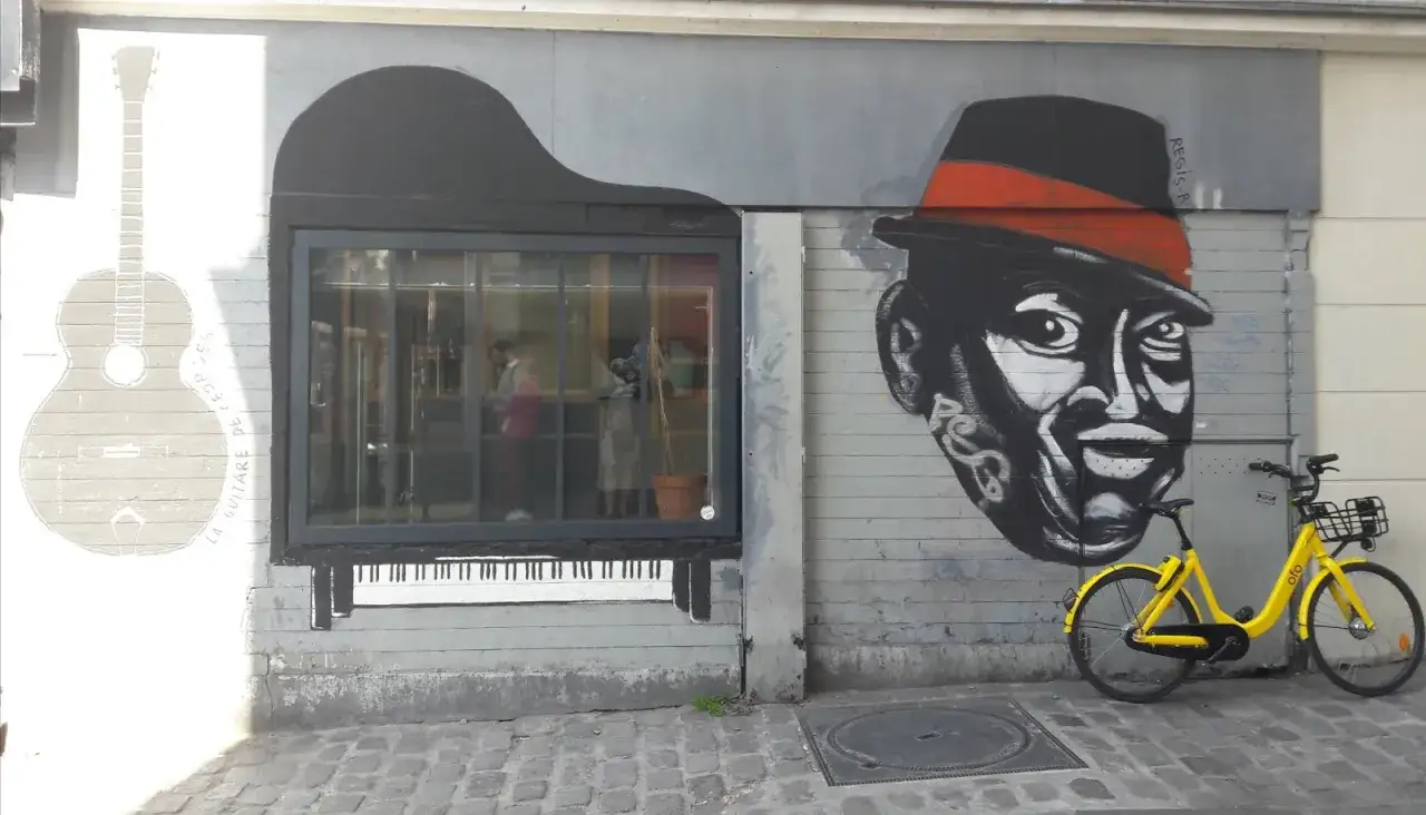 Muzyczna ściana w 13 dzielnicy Paryża: gitara, fortepian i portret mężczyzny w kapeluszu. Obok żółty rower.