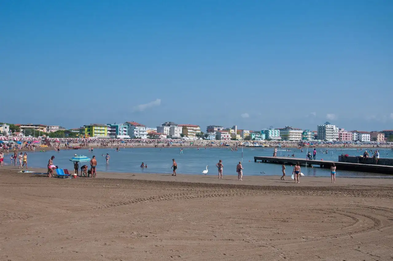 Tłum ludzi na plaży i w wodzie, z hotelami w tle. Czy Rimini jest bezpieczne? Wygląda na spokojne, z rodzinami i turystami cieszącymi się słońcem.