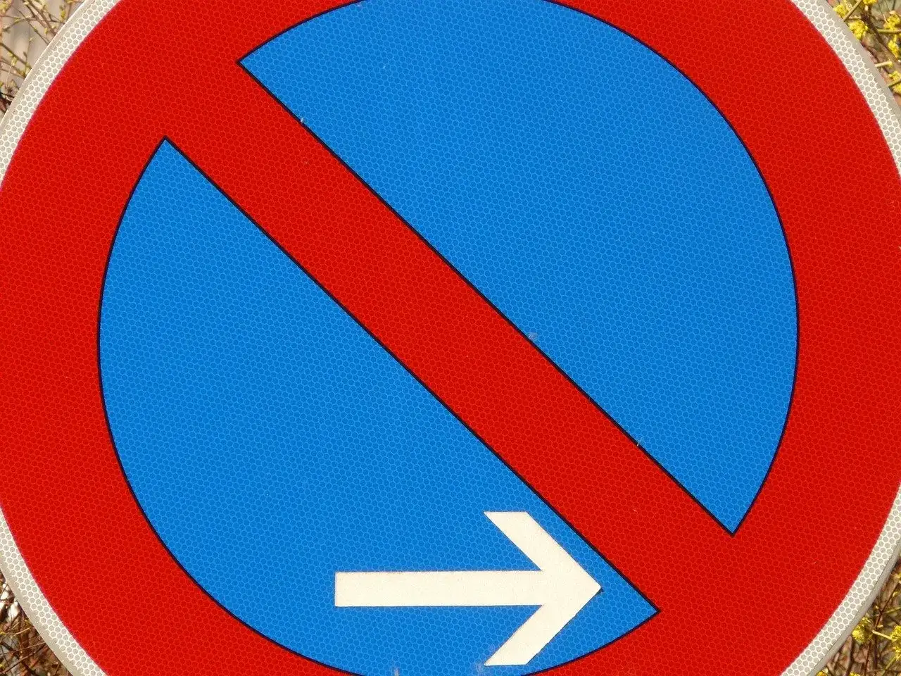 Znak zakazu parkowania przed znakiem, z białą strzałką wskazującą w prawo.