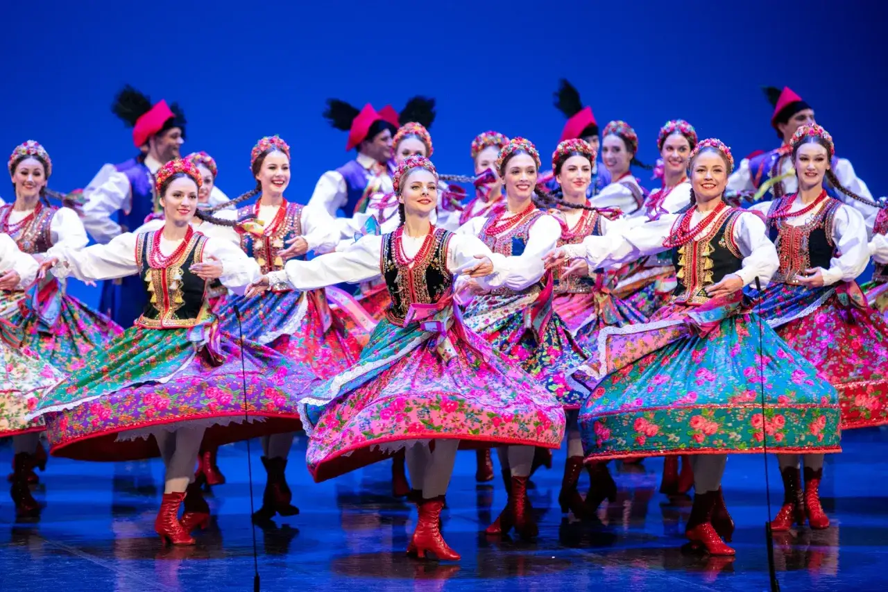 Tancerki w barwnych strojach, prezentujące muzykę ludową Mazowsza, wirują na scenie w rytm tradycyjnych melodii.