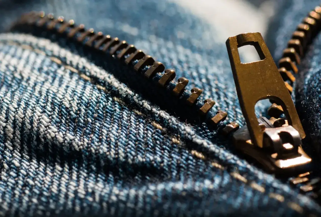 Zbliżenie na metalowy zamek błyskawiczny w dżinsach. Pomyśl, kiedy wynaleziono zamek błyskawiczny, by ułatwić życie!