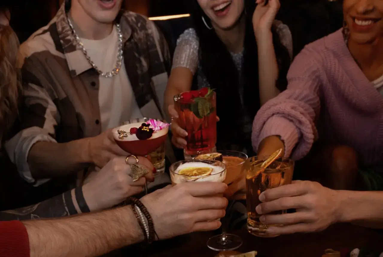 Grupa przyjaciół wznosi toast kolorowymi drinkami z wódką.