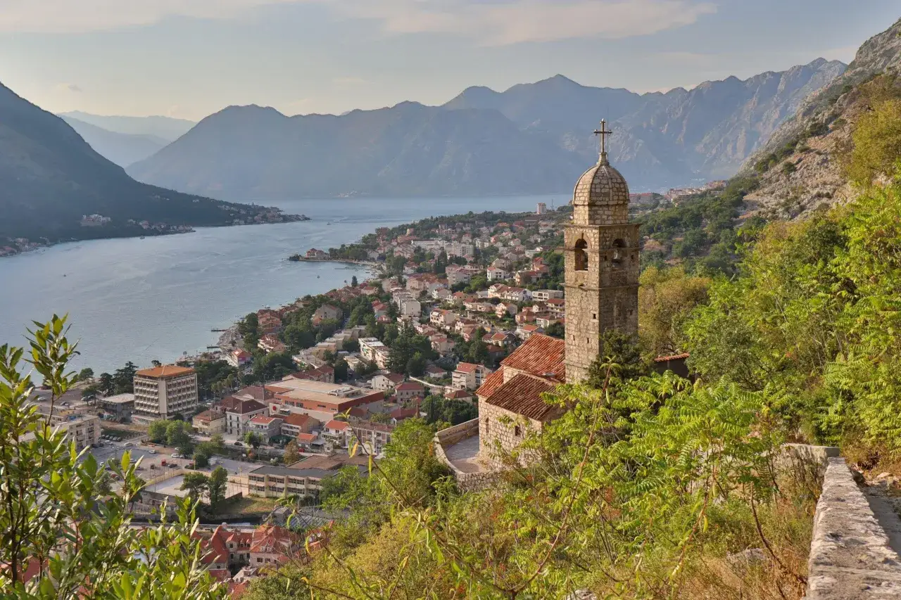 Widok na Zatokę Kotorską i miasto. W oddali góry, na pierwszym planie wieża kościelna. Czarnogóra ceny noclegów i wyżywienia są przystępne.