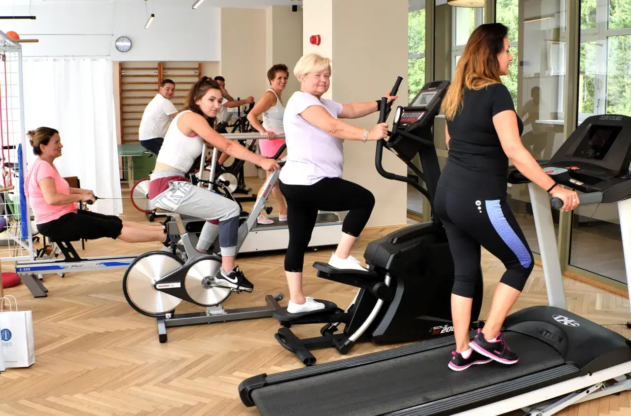 Fizjoterapia ambulatoryjna: jakie zabiegi? Kobiety ćwiczą na rowerkach, bieżniach i stepperach, rehabilitując się w przyjaznej atmosferze.