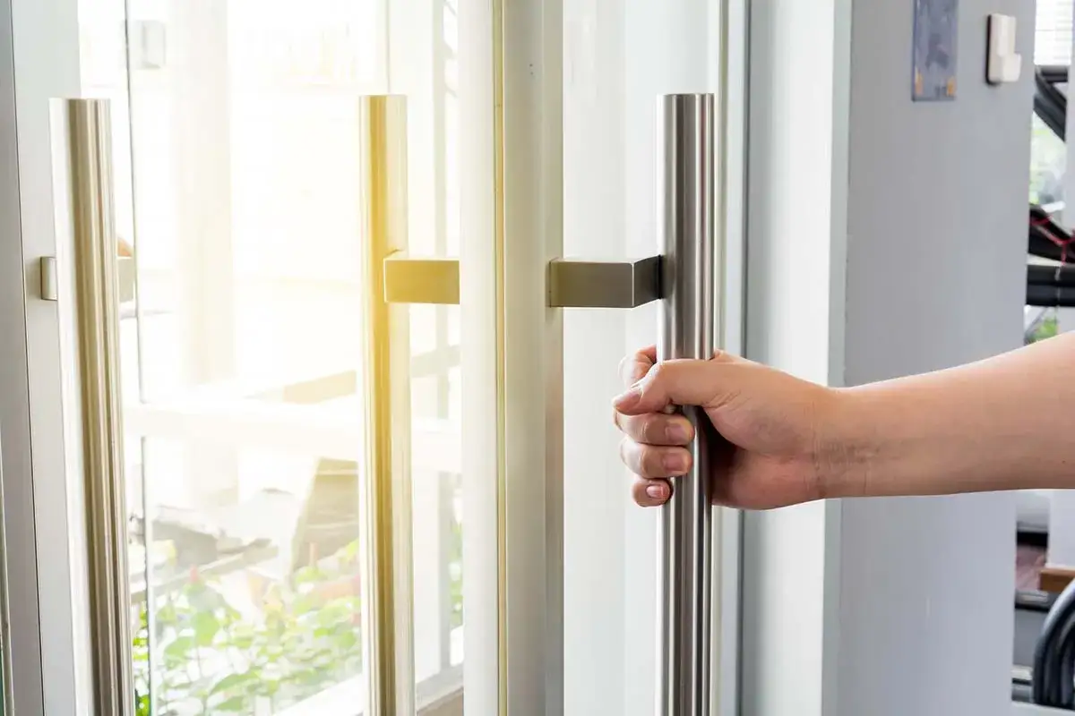 Dłoń chwyta za metalowy pochwyt drzwi, otwierając przejście na jasną, słoneczną stronę.