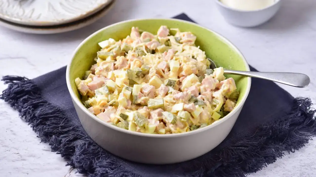 Sałatka z selera konserwowego z szynką, jajkiem i og&oacute;rkiem, wymieszana z majonezem, prezentuje się apetycznie w zielonej misce.