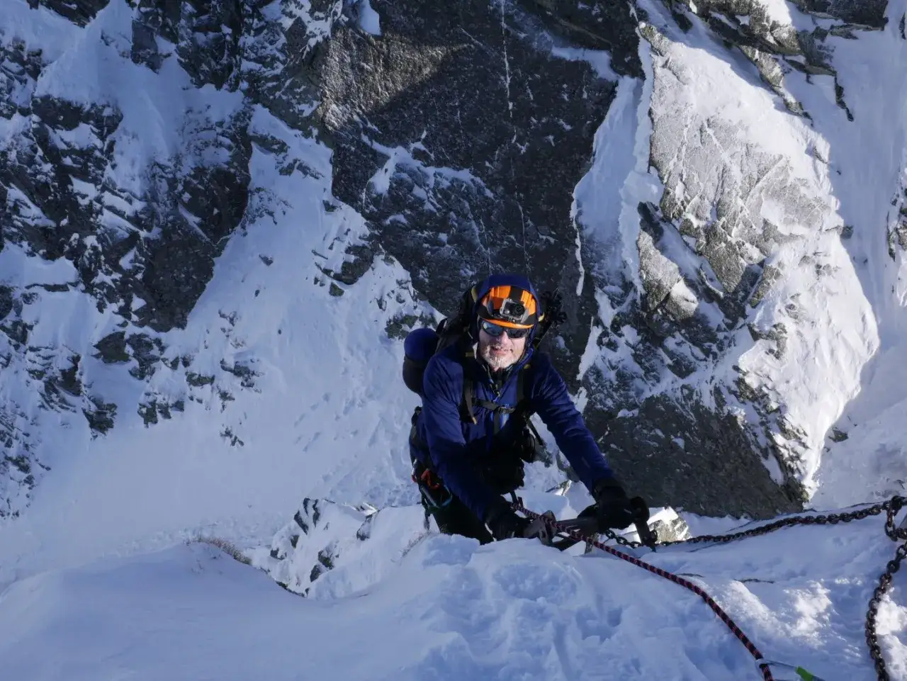 Wspinaczka zimą na Orlą Perć. Mężczyzna w kasku i okularach wspina się po skalnej ścianie, trzymając się łańcucha i liny.