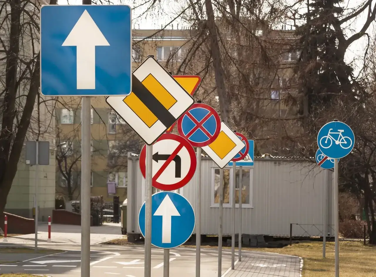 Różnorodne znaki drogowe, w tym zakaz skrętu, pierwszeństwo i ścieżka rowerowa, prezentują swoje wymiary w słoneczny dzień.