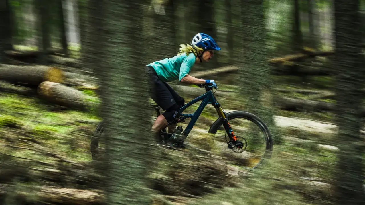 Kobieta w kasku śmiga na rowerze g&oacute;rskim 29 przez leśny szlak, otoczona rozmytymi drzewami i zielenią.