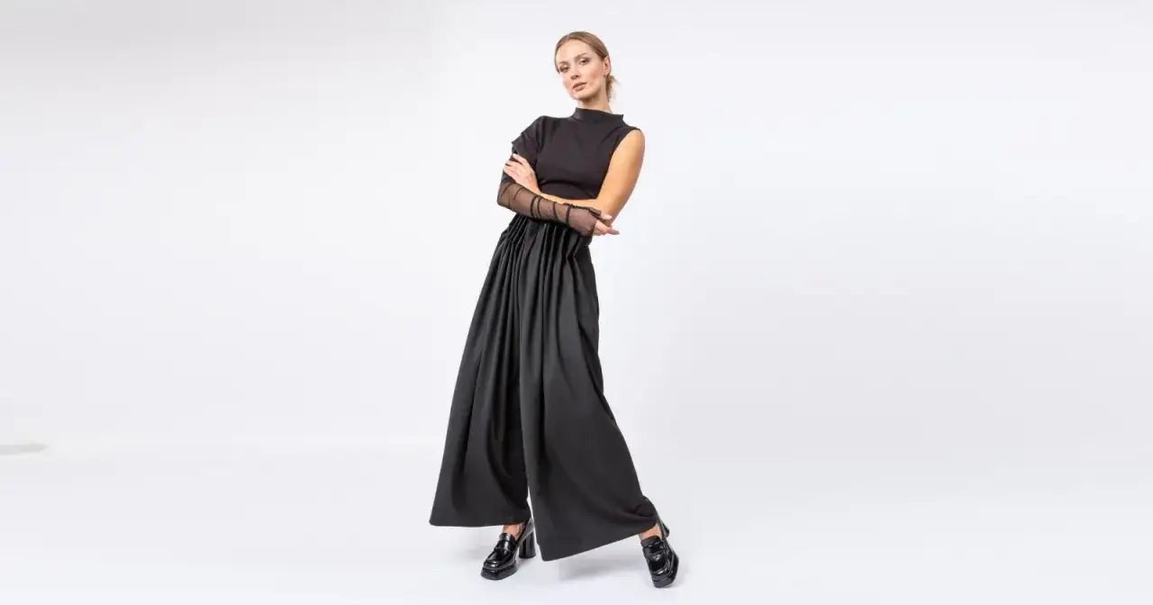 Elegancka kobieta w czerni, idealna stylizacja w czym do teatru. Szerokie spodnie i bluzka z siateczkowymi rękawami.