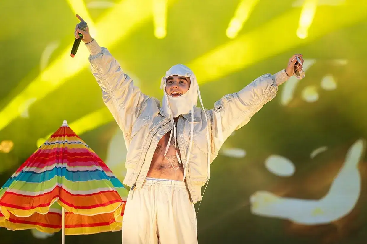 Artysta na scenie z mikrofonem, w białej kurtce i spodniach. Obok kolorowy parasol. Ile lat ma Mata?