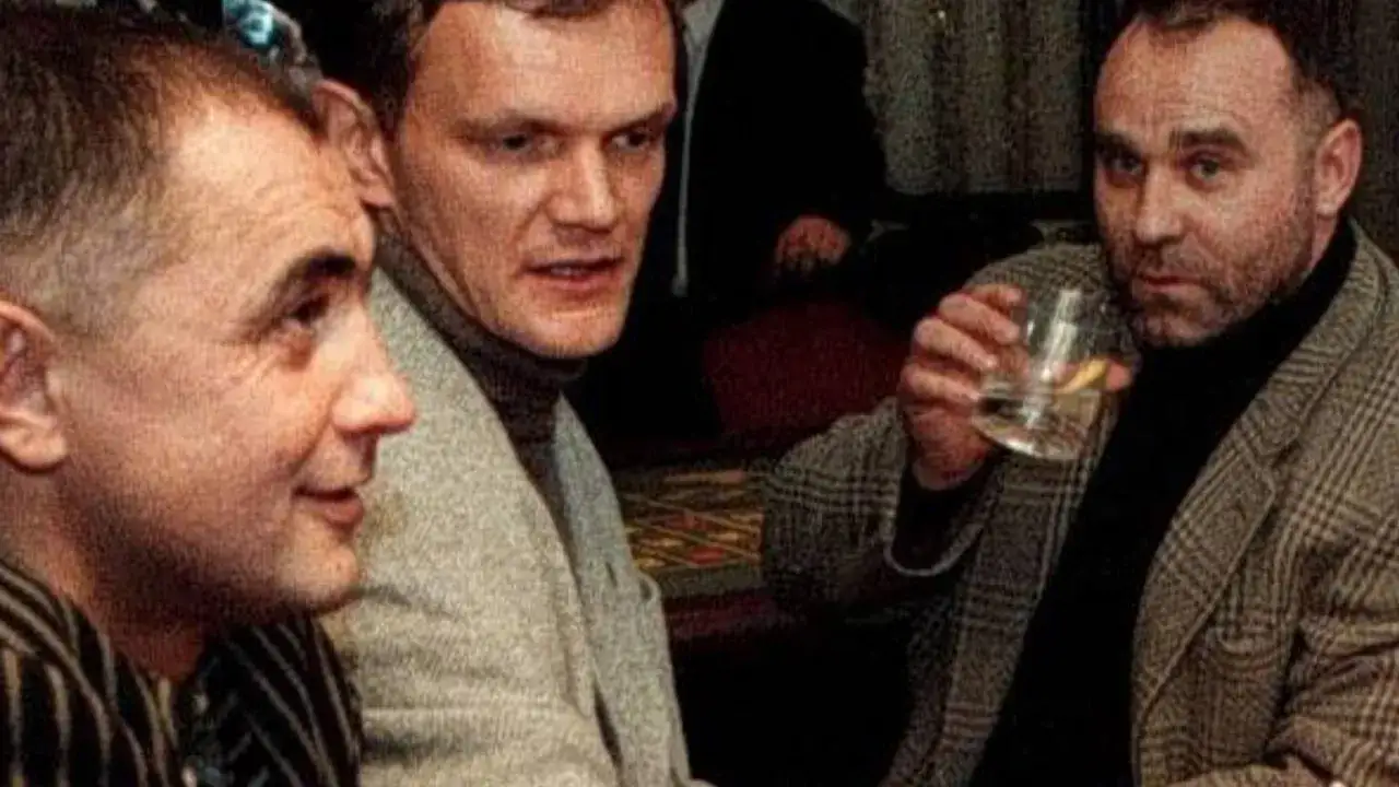 Trzech mężczyzn w eleganckich ubraniach, jeden z nich trzyma szklankę. Może to początek historii 