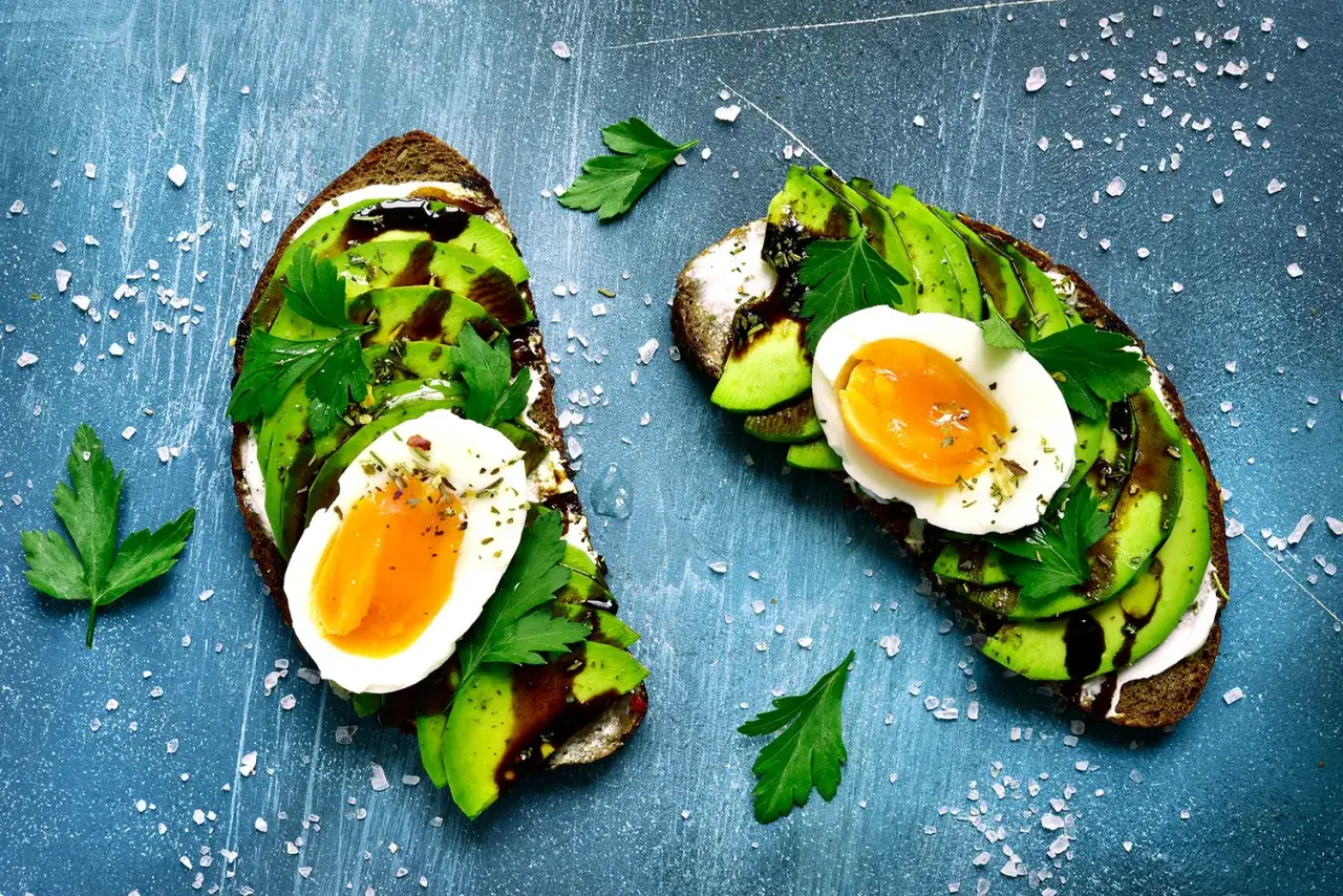 Dwa tosty z awokado i jajkiem na twardo, posypane ziołami i solą. Idealne na śniadanie w stylu dieta bezglutenowa przepisy.