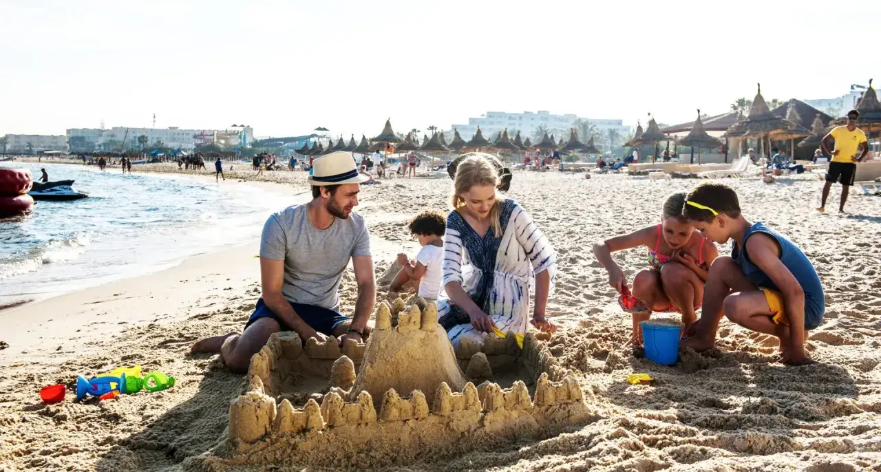 Rodzina buduje zamek z piasku na plaży. Słoneczna, sierpniowa pogoda w Tunezji sprzyja wakacyjnym zabawom.