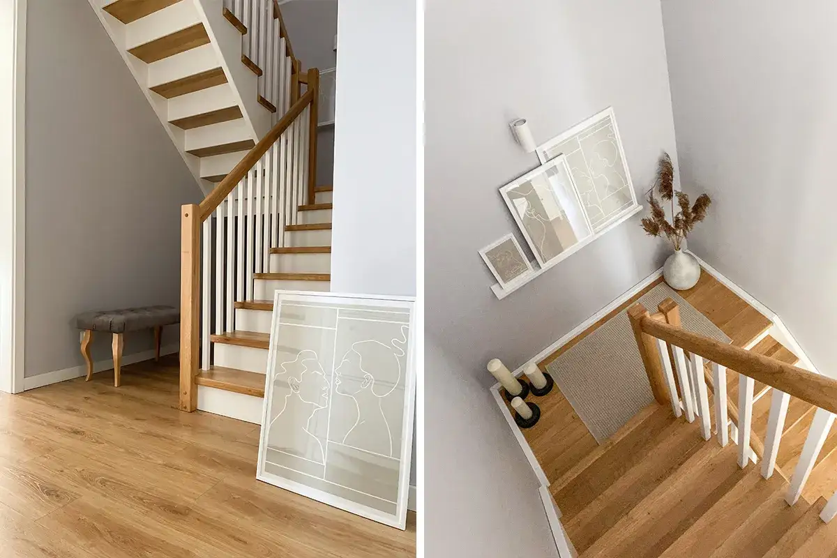 Drewniana boazeria na klatce schodowej, białe stopnie i balustrada tworzą przytulną atmosferę. Obok stoi ławka i grafika.