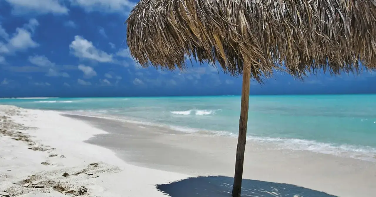 Słomiany parasol na białej plaży, turkusowe morze i błękitne niebo. Idealne miejsce, by zastanowić się, kiedy jechać na Kubę.