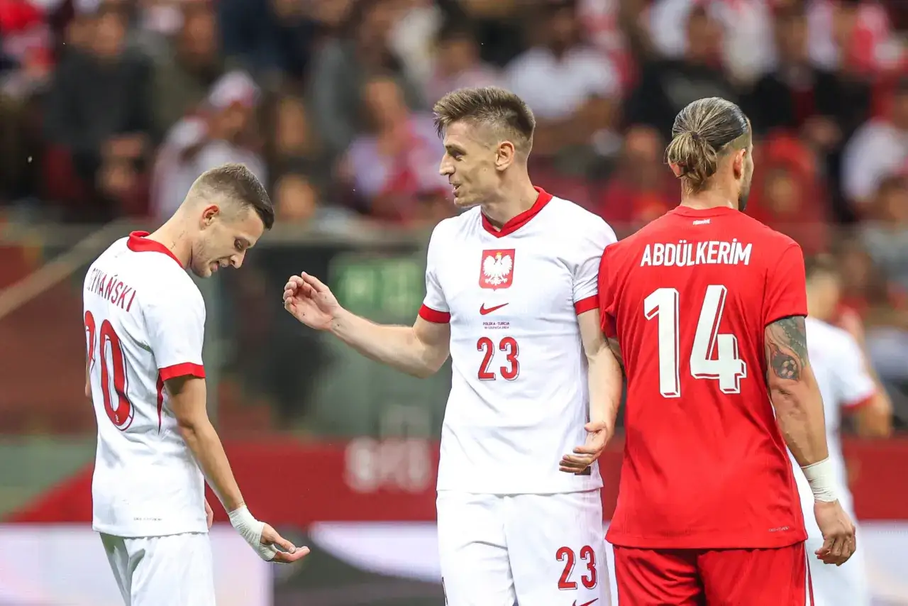 Piłkarze ze Stambułu w akcji. Dwóch zawodników w białych strojach reprezentacji Polski, jeden w czerwonym stroju Turcji.