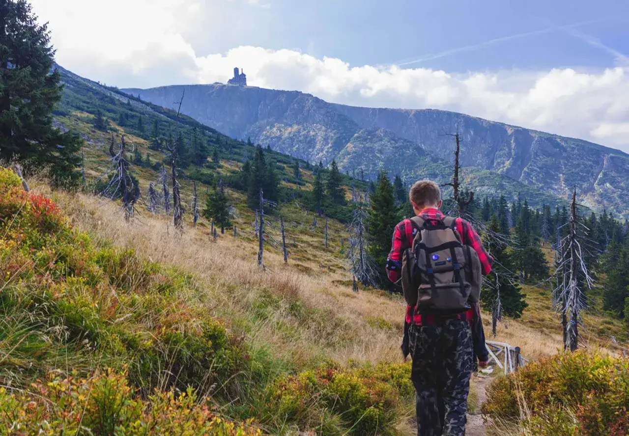 Młody turysta z plecakiem idzie szlakiem przez jesienne g&oacute;ry. Warto wiedzieć, co zabrać w g&oacute;ry, by cieszyć się widokami.